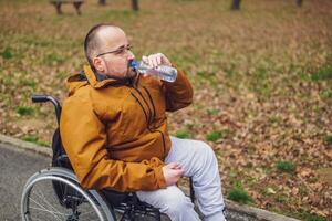 paraplegico portatori di handicap uomo nel sedia a rotelle è godendo all'aperto e potabile acqua. foto