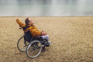 posteriore Visualizza Immagine di paraplegico portatori di handicap uomo nel sedia a rotelle di il lago. lui è godendo all'aperto. foto