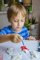 il ragazzo disegna e vernici gesso figure con un' spazzola e guazzo su un' pezzo di carta. foto