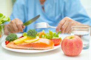 asiatico anziano donna paziente mangiare salmone bistecca prima colazione con verdura salutare cibo nel Ospedale. foto