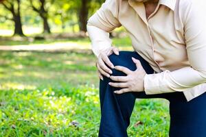 anziano donna a piedi nel il parco lei aveva acuto ginocchio dolore. osteoartrite concetto ginocchio infiammazione nel il anziano. Salute cura. copia spazio foto