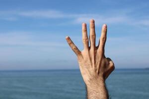 mano fare, mostrare numero quattro gesto simbolo su blu estate cielo natura sfondo. Esprimere a gesti numero 4. numero quattro nel cartello linguaggio. quattro dita su foto