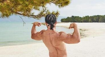 giovane muscolare uomo esercizio su il spiaggia, giovane muscolare uomo fare bodybuilding esercizi su il spiaggia, atletico giovane uomo su il spiaggia foto