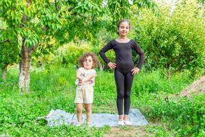 bella ragazza insegnamento yoga per sua sorella, poco ragazze fare yoga esercizi nel il giardino foto