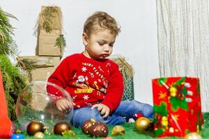 il poco bambino giocando con Natale decorazioni nel studio, poco bambino con Natale palla foto