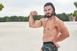 giovane muscolare uomo esercizio su il spiaggia, giovane muscolare uomo fare bodybuilding esercizi su il spiaggia, atletico giovane uomo su il spiaggia foto