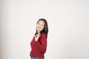 giovane asiatico donna nel rosso maglietta sorridente e mostrando va bene cartello isolato su bianca sfondo foto