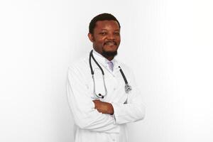 sorridente nero barbuto medico uomo attraversato braccia nel bianca cappotto con stetoscopio, bianca sfondo foto