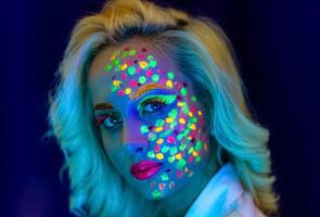 ritratto di un' donna con dipinto viso, donna con uv trucco nel studio, ritratto di un' donna nel carnevale maschera, il donna è decorato nel un' ultravioletto polvere foto