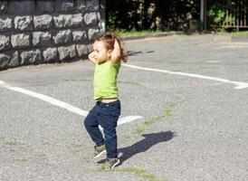 contento poco ragazzo giocando nel il parco, lungo capelli ragazzo nel il parco foto