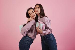 festeggiare insieme. giovani donne che si divertono in studio con sfondo rosa. adorabili gemelli foto