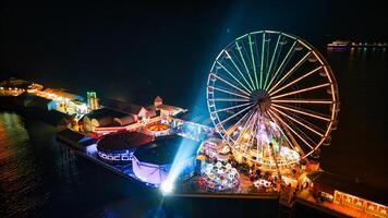 aereo notte Visualizza di un' vivace divertimento parco con un' grande Ferris ruota, illuminato attrazioni, e lungomare Posizione nel backpool, Inghilterra. foto