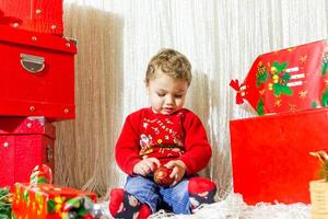 il poco bambino giocando con Natale decorazioni nel studio, poco bambino con Natale palla foto