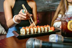 persona Tenere bastoncini al di sopra di piatto di Sushi foto