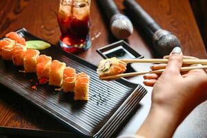 persona Tenere bastoncini al di sopra di piatto di Sushi foto