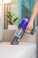 donna pulizia divano con cordless vuoto più pulito. casalinga utilizzando senza fili aspirapolvere per grande pulizia casa. lavori di casa, pulizie di casa, faccende domestiche, rimuove polvere, domestico igiene e quotidiano routine foto