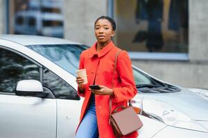 utilizzando smartphone mentre in attesa. donna su il elettrico macchine caricare stazione a giorno. marca nuovo veicolo. foto