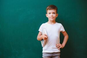 indietro per scuola concetto. scuola bambino nel classe. contento ragazzo contro verde lavagna. inteligente bambino nel aula. idea e formazione scolastica concetto foto