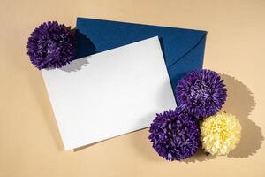 bellissimo poco viola fiori su postale blu Busta su beige sfondo, vuoto carta Nota copia spazio per testo, primavera volta, saluto carta per vacanza. fiore consegna concetto foto