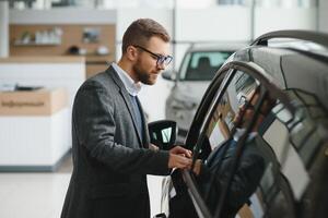 contento proprietario di un' nuovo macchina. emotivo bello uomo nel casuale Abiti è felice, acquisto un' auto nel il concessionaria. foto