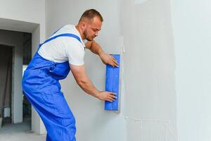 un' generale lavoratore nel tuta da lavoro usi un' cazzuola per copertina il parete con cemento foto