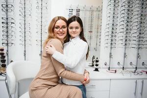 bellissimo poco ragazza nel ottica memorizzare insieme con mamma scegliere nuovo occhiali. foto