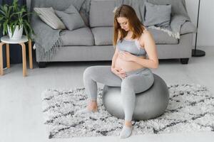 giovane incinta donna esercizio yoga con in forma palla a casa. salutare gli sport gravidanza concetto foto