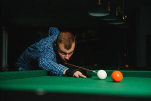 giovane bello uomo pendente al di sopra di il tavolo mentre giocando snooker foto