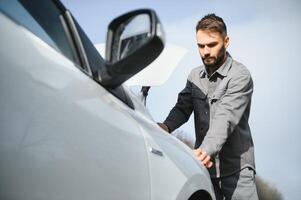 giovane irritato casuale uomo provando per fix il suo rotto auto all'aperto. uomo in attesa per rimorchio servizio per Aiuto auto incidente su il strada. ciglio della strada assistenza concetto. foto