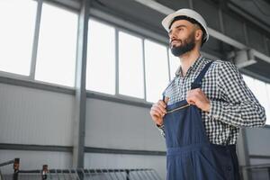 ritratto di professionale pesante industria ingegnere lavoratore indossare sicurezza uniforme, difficile cappello sorridente. nel il sfondo sfocata grande industriale fabbrica. foto