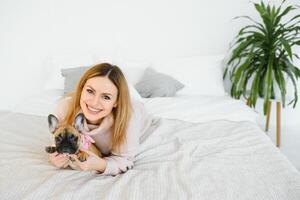 allegro giovane donna Tenere sua grande cucciolo con nero naso e ridendo. interno ritratto di sorridente ragazza in posa con francese bulldog foto