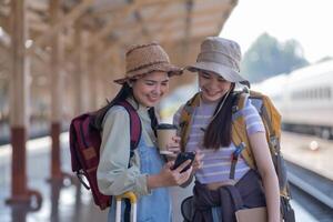 Due giovane asiatico amici ragazze con zaini a ferrovia stazione in attesa per treno, Due bellissimo donne a piedi lungo piattaforma a treno stazione foto