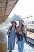 Due giovane asiatico amici ragazze con zaini a ferrovia stazione in attesa per treno, Due bellissimo donne a piedi lungo piattaforma a treno stazione foto