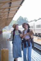 Due giovane asiatico amici ragazze con zaini a ferrovia stazione in attesa per treno, Due bellissimo donne a piedi lungo piattaforma a treno stazione foto