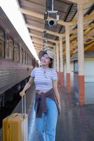 giovane donna con valigia aspetta a il la metropolitana stazione mentre il treno arriva, turismo e viaggio nel il estate. vacanze per il alunno. opera e viaggio foto