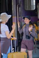 Due giovane asiatico amici ragazze con zaini a ferrovia stazione in attesa per treno, Due bellissimo donne a piedi lungo piattaforma a treno stazione foto