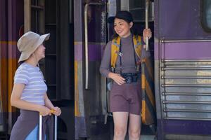 Due giovane asiatico amici ragazze con zaini a ferrovia stazione in attesa per treno, Due bellissimo donne a piedi lungo piattaforma a treno stazione foto