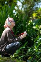 bellissimo giovane artista donna assunzione foto nel fiori giardino. giovane carino ragazza trasportare il telecamera nel il giardino