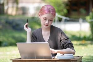 donna Lavorando a il il computer portatile nel il Giardino dietro la casa con un' lotto di verde, il computer portatile e ritratto di donna nel parco per formazione scolastica foto