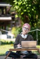 donna Lavorando a il il computer portatile nel il Giardino dietro la casa con un' lotto di verde, il computer portatile e ritratto di donna nel parco per formazione scolastica foto