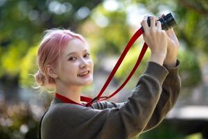 bellissimo giovane artista donna assunzione foto nel fiori giardino. giovane carino ragazza trasportare il telecamera nel il giardino