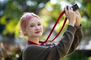 bellissimo giovane artista donna assunzione foto nel fiori giardino. giovane carino ragazza trasportare il telecamera nel il giardino