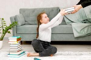 un' poco ragazza seduta su il pavimento tra libri prende libri tenuto su di un adulto foto