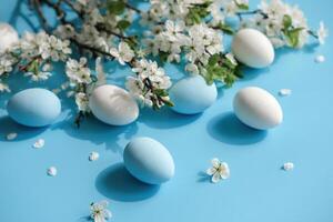 bianca e blu uova in mezzo ciliegia fiori su un' vivace blu fondale significare Pasqua e primavera foto