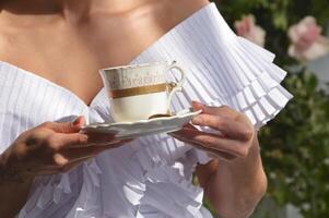 un' sposa ragazza nel un' bianca vestito detiene un' tazza di tè o caffè nel sua mani. Da donna mani con un' tazza. foto