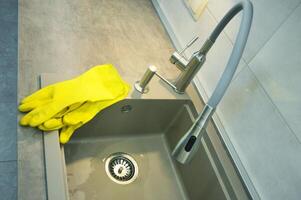 cucina Lavello con flessibile rubinetto senza piatti. Là siamo giallo pulizia guanti su il bordo. foto