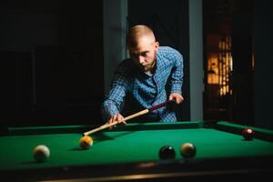 giovane bello uomo pendente al di sopra di il tavolo mentre giocando snooker foto