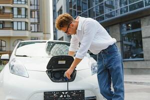 uomo Tenere energia ricarica cavo per elettrico auto nel all'aperto auto parco. e lui S andando per Collegare il auto per il ricarica stazione nel il parcheggio lotto vicino il shopping centro foto