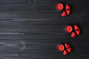 rosso caramelle nel un' modulo di cuore e rosso candele su il buio blu di legno tavolo. sfondo per saluto carta su San Valentino giorno con posto per testo. foto