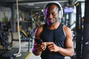 atletico uomo in piedi nel un' Palestra ascoltando per musica utilizzando senza fili cuffie foto